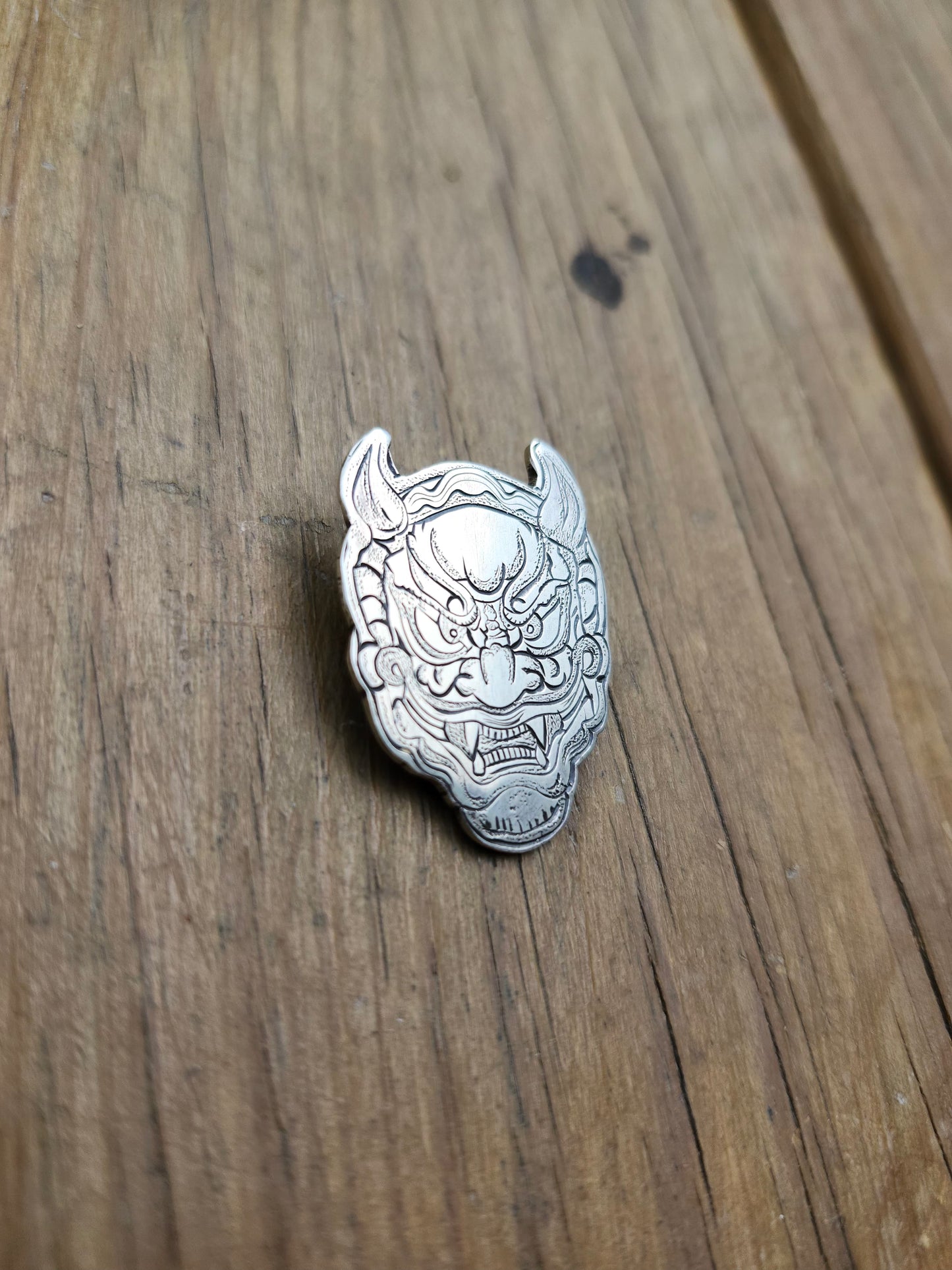 Detailed close-up of the engraved lines and textures on a sterling silver Oni mask pendant.