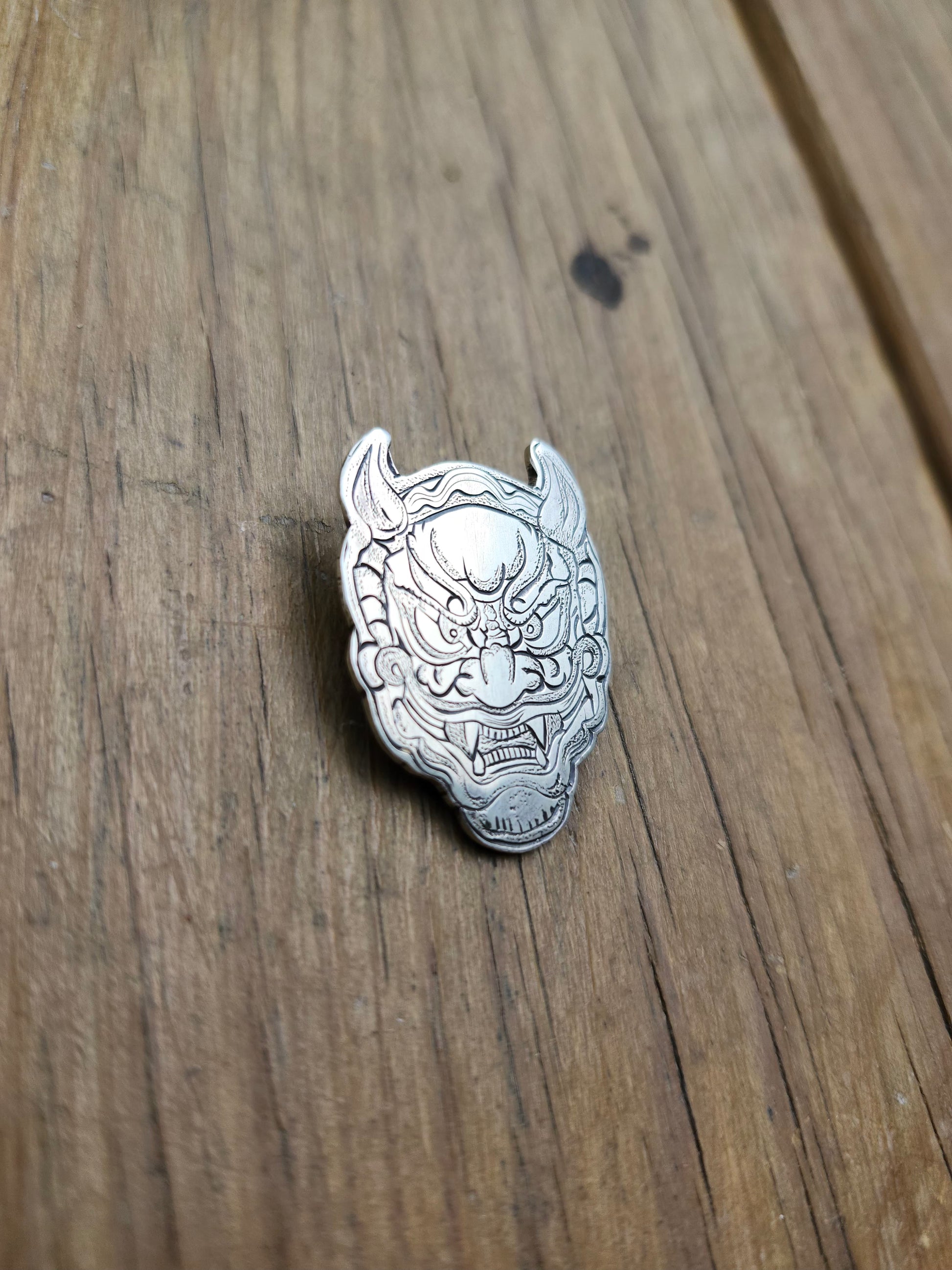 Detailed close-up of the engraved lines and textures on a sterling silver Oni mask pendant.
