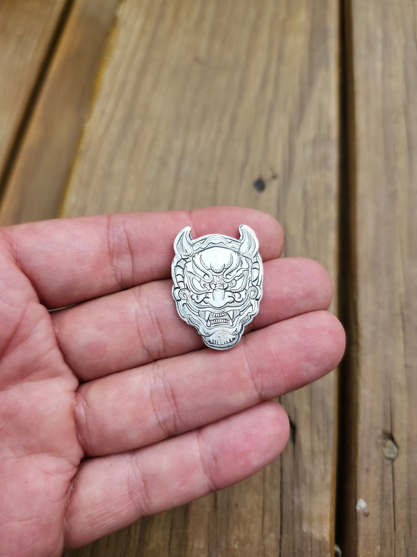 Detailed close-up of the engraved lines and textures on a sterling silver Oni mask pendant.