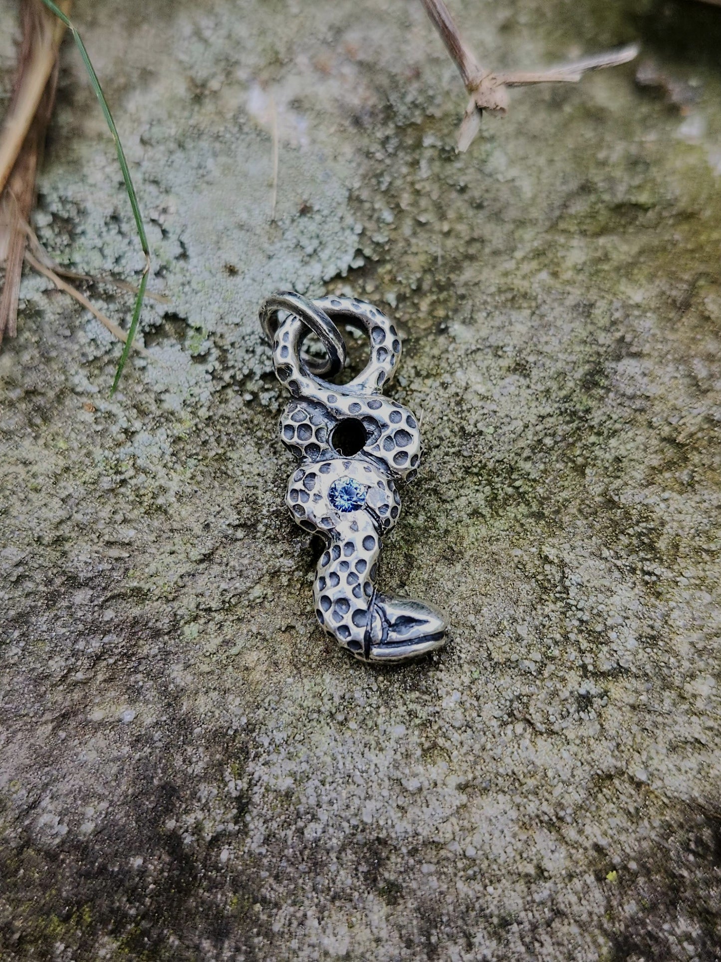 Sapphire snake pendant on mossy stone background, artisan jewelry