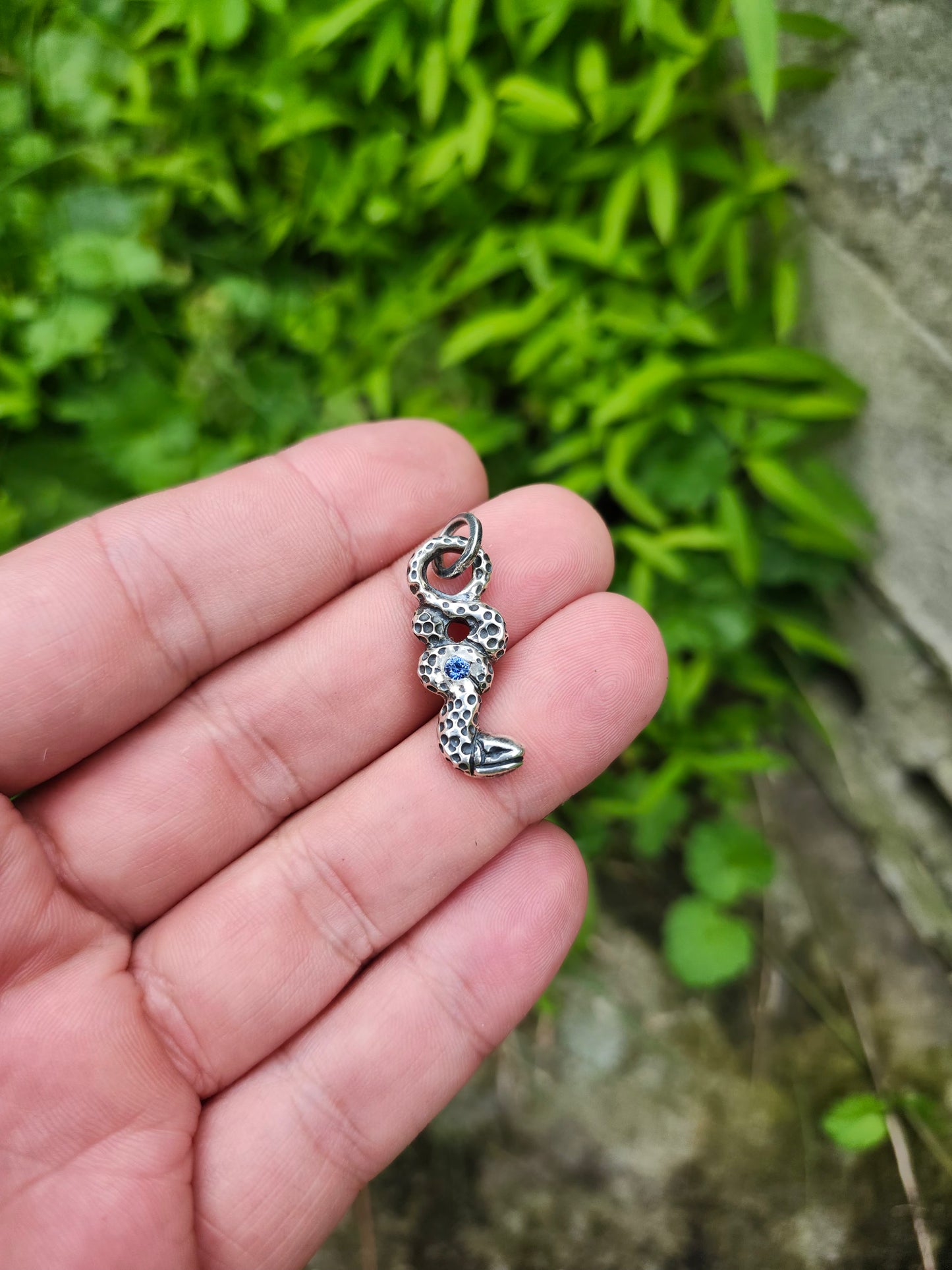 Hand holding silver serpent pendant with sapphire gemstone