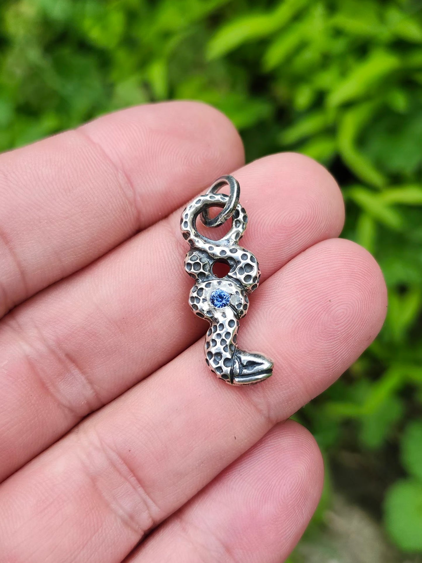 Hand holding silver serpent pendant with sapphire gemstone