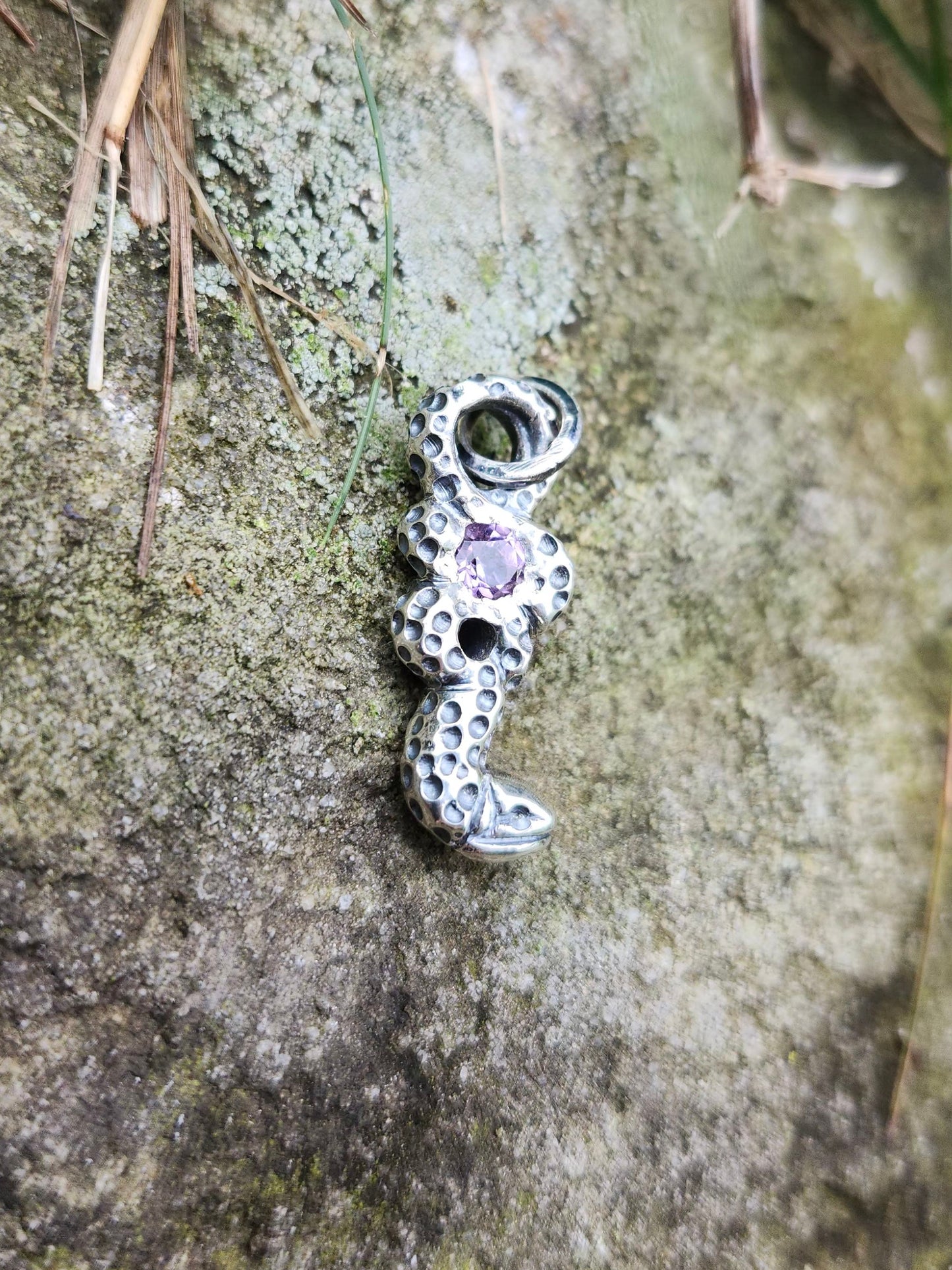 Amethyst snake pendant on mossy stone background, artisan jewelry