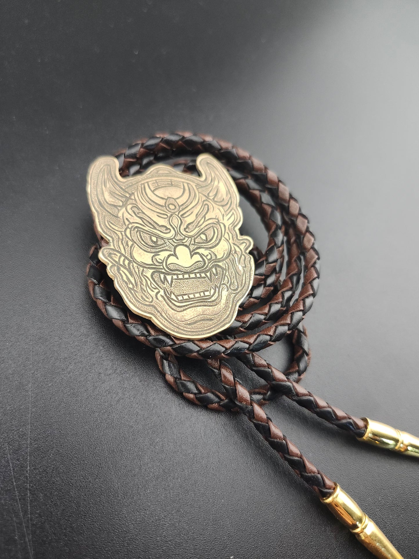 Oni Mask Bolo Tie – Hand-Engraved Brass on Braided Leather