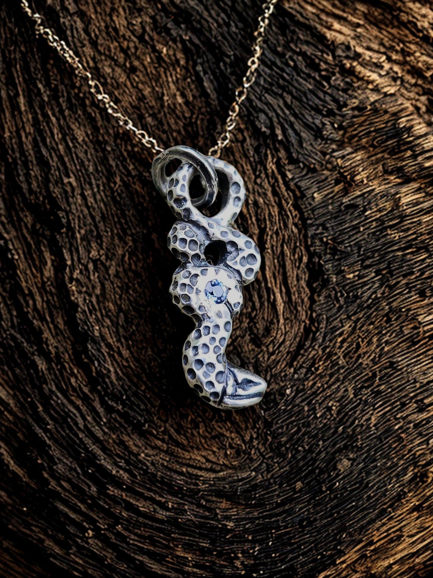 Sapphire snake pendant on natural wood grain background, nature, artisan jewelry