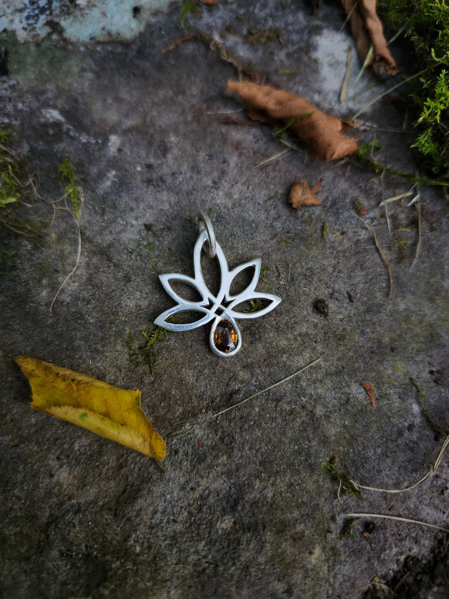 Close-up of hand-carved Celtic-style cannabis leaf pendant in sterling silver with a pear-cut golden zircon,