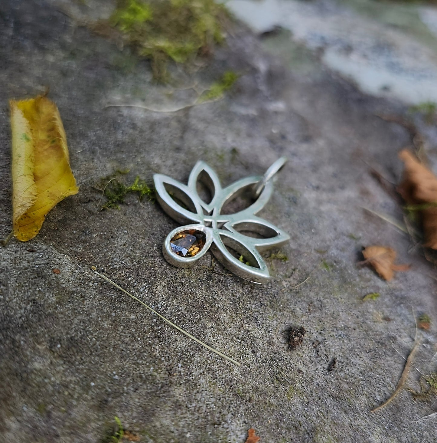 Silver leaf-shaped pendant with a gemstone on a textured stone surface