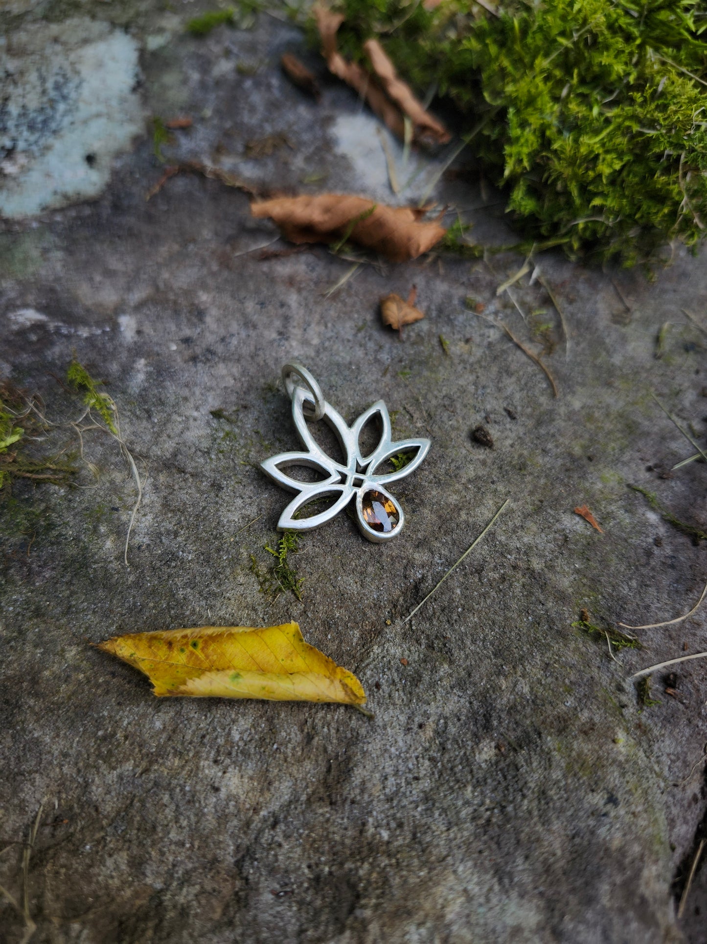 Close-up of hand-carved Celtic-style cannabis leaf pendant in sterling silver with a pear-cut golden zircon,