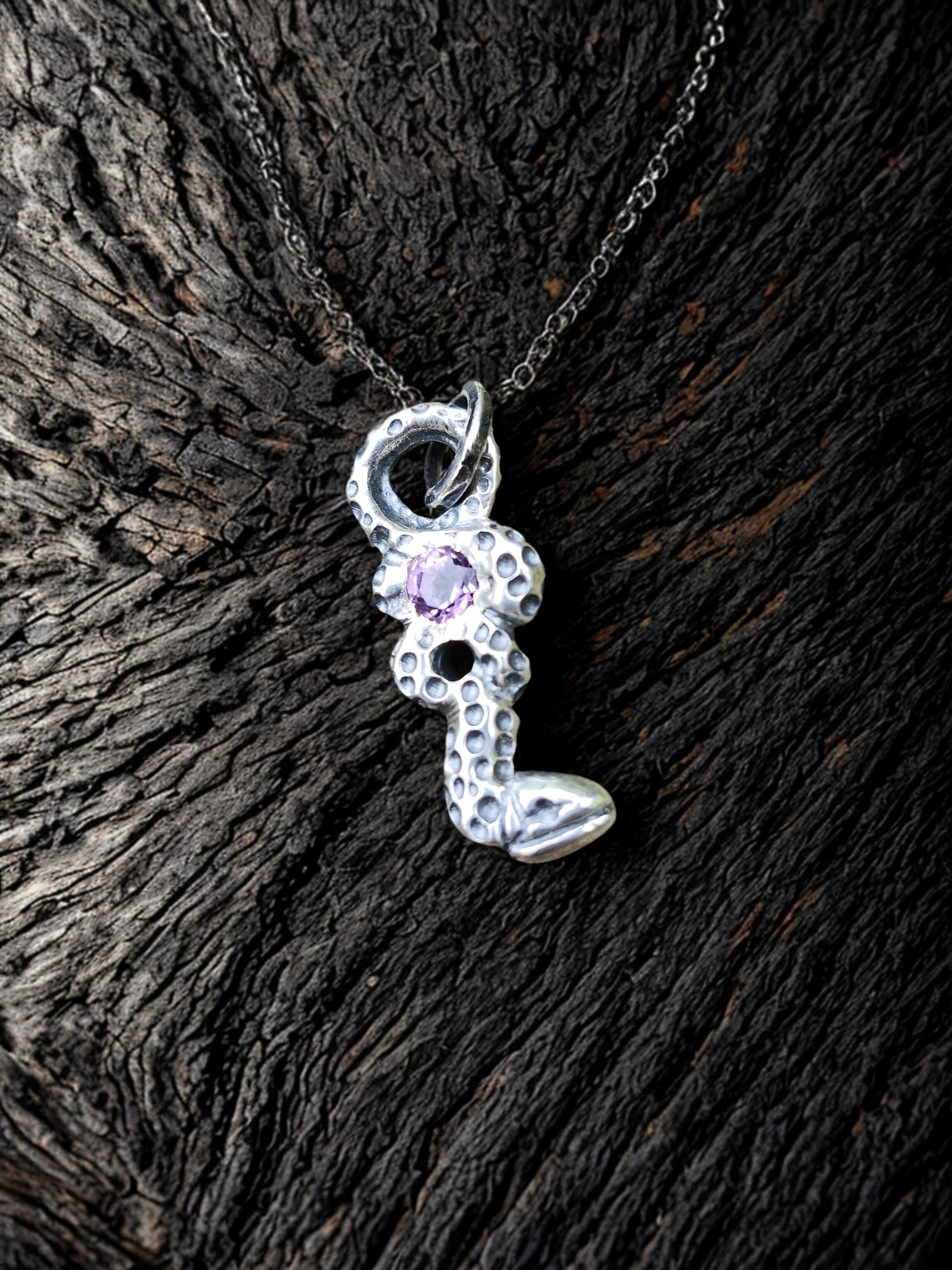Amethyst’s snake pendant on natural wood grain background, nature, artisan jewelry
