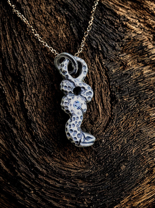 Sapphire snake pendant on natural wood grain background, nature, artisan jewelry