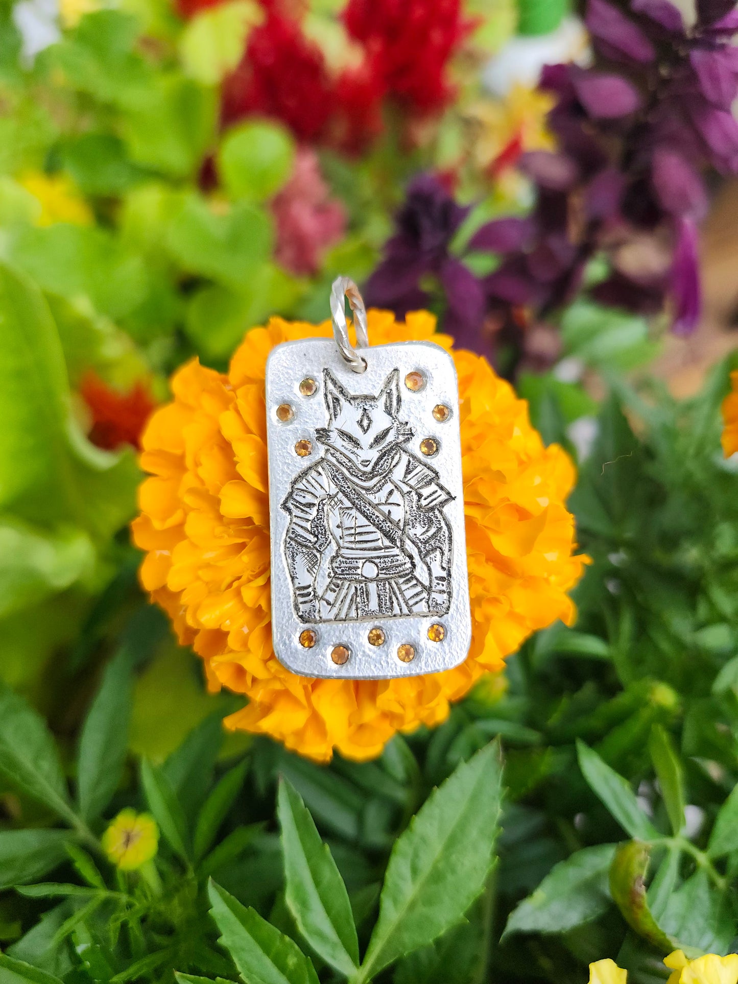 Kitsune pendant resting on a marigold, showcasing opal details and engraved armor
