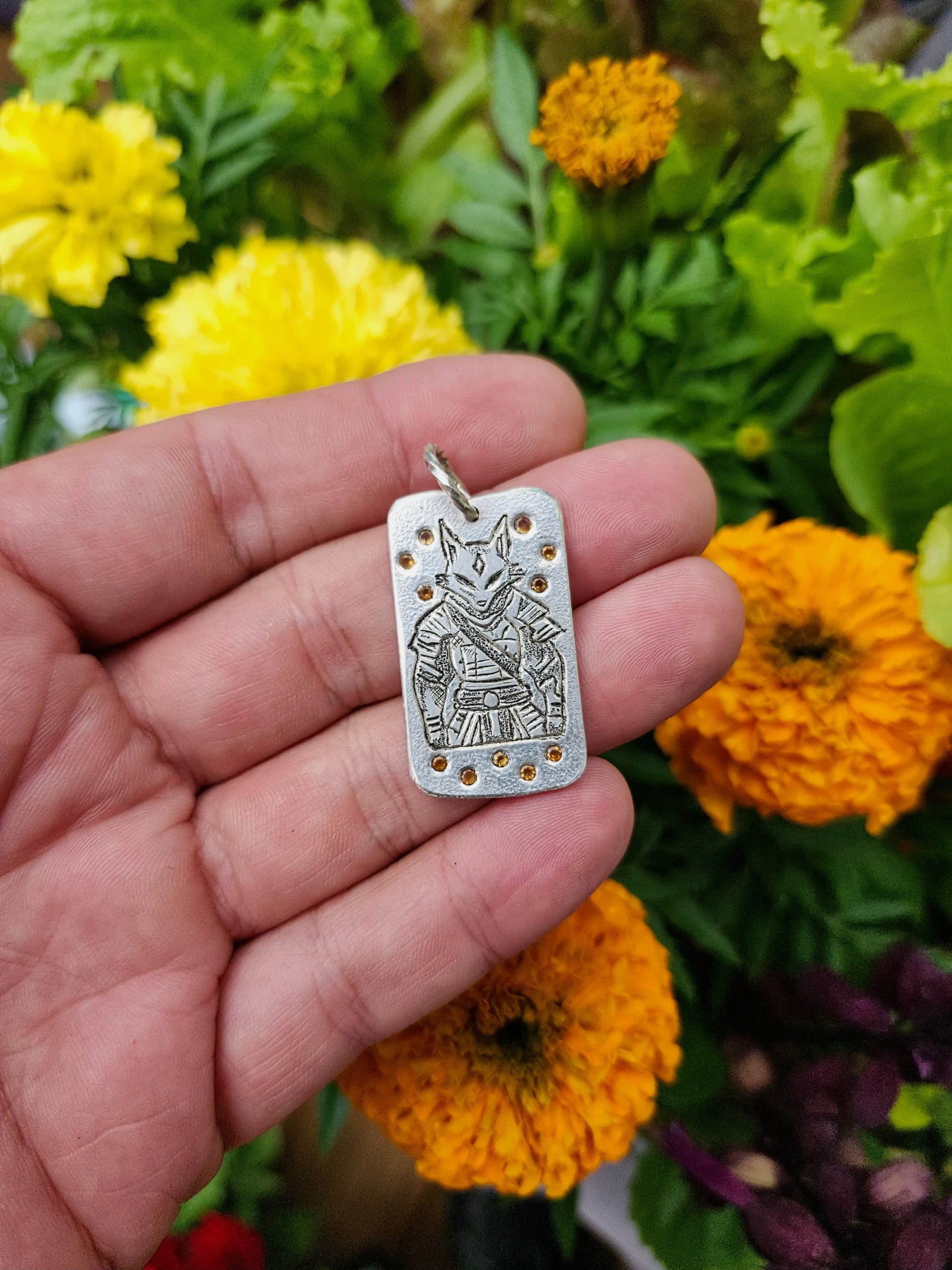 Hand holding sterling silver Kitsune warrior pendant with fire opals, floral background